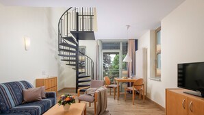 Un salon moderne avec un escalier en colimaçon, un canapé, une table basse avec un livre, un téléviseur et un coin repas avec des chaises et une table.