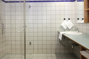 A bathroom with a glass shower enclosure, a sink with a mirror, and a towel rack with two towels. - Apartments, Gohren (Göhren)