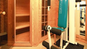 Un gimnasio con una máquina de pesa rusa, una puerta que da a una sauna y una pared de madera.