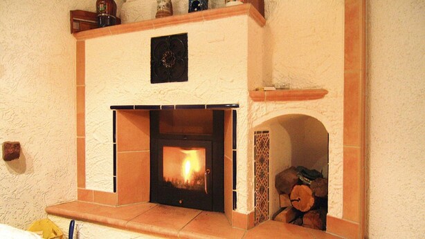 Una chimenea con marco de piedra, fuego ardiendo en su interior y leña apilada en el frente.