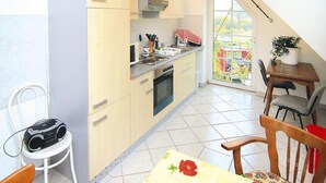 Cocina compacta con estufa, microondas y fregadero, zona de comedor con mesa y sillas, y vista a un jardín a través de un ventanal grande.