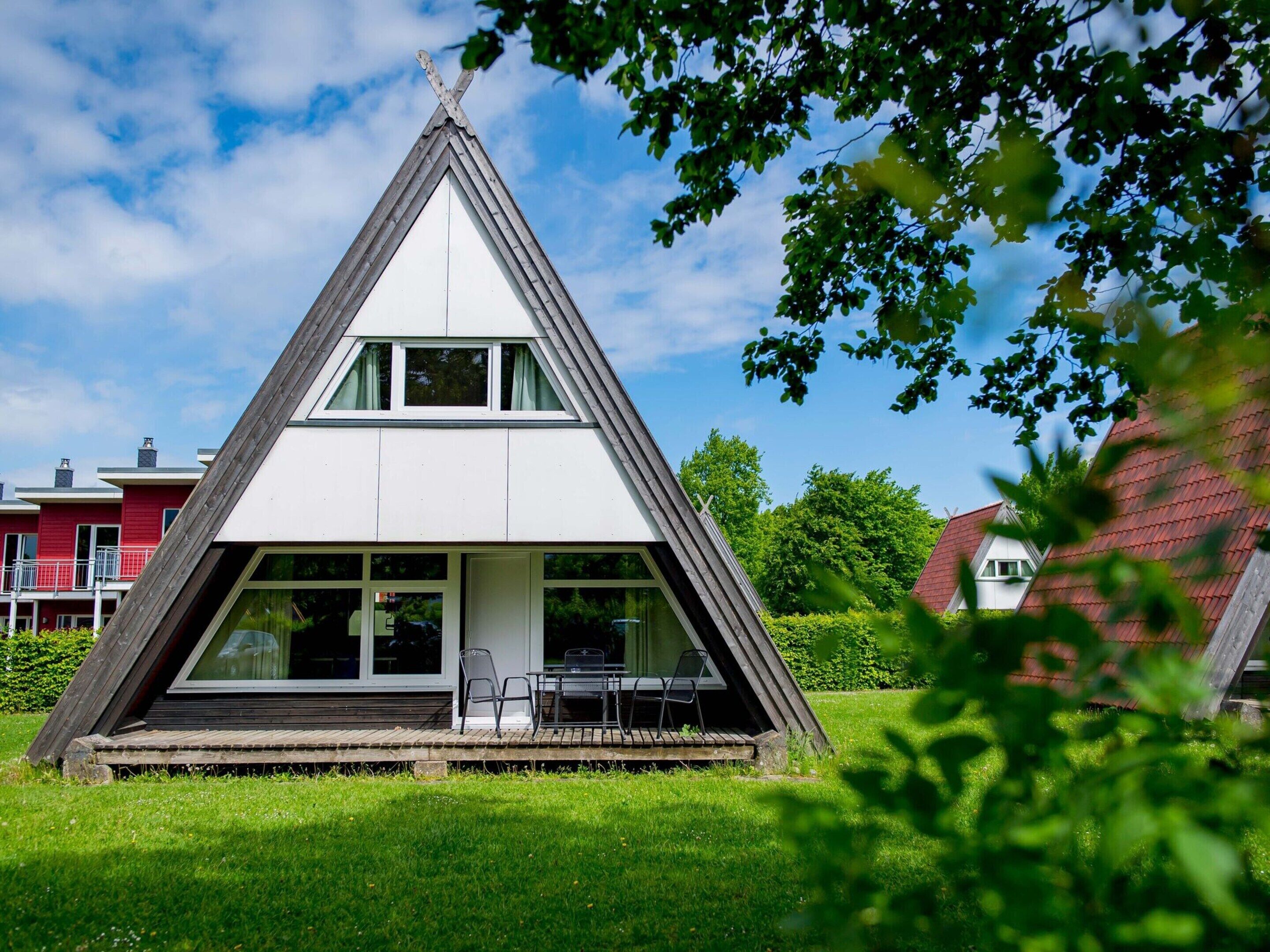 Un bâtiment triangulaire doté d’un toit plat et d’une petite terrasse avec des chaises.