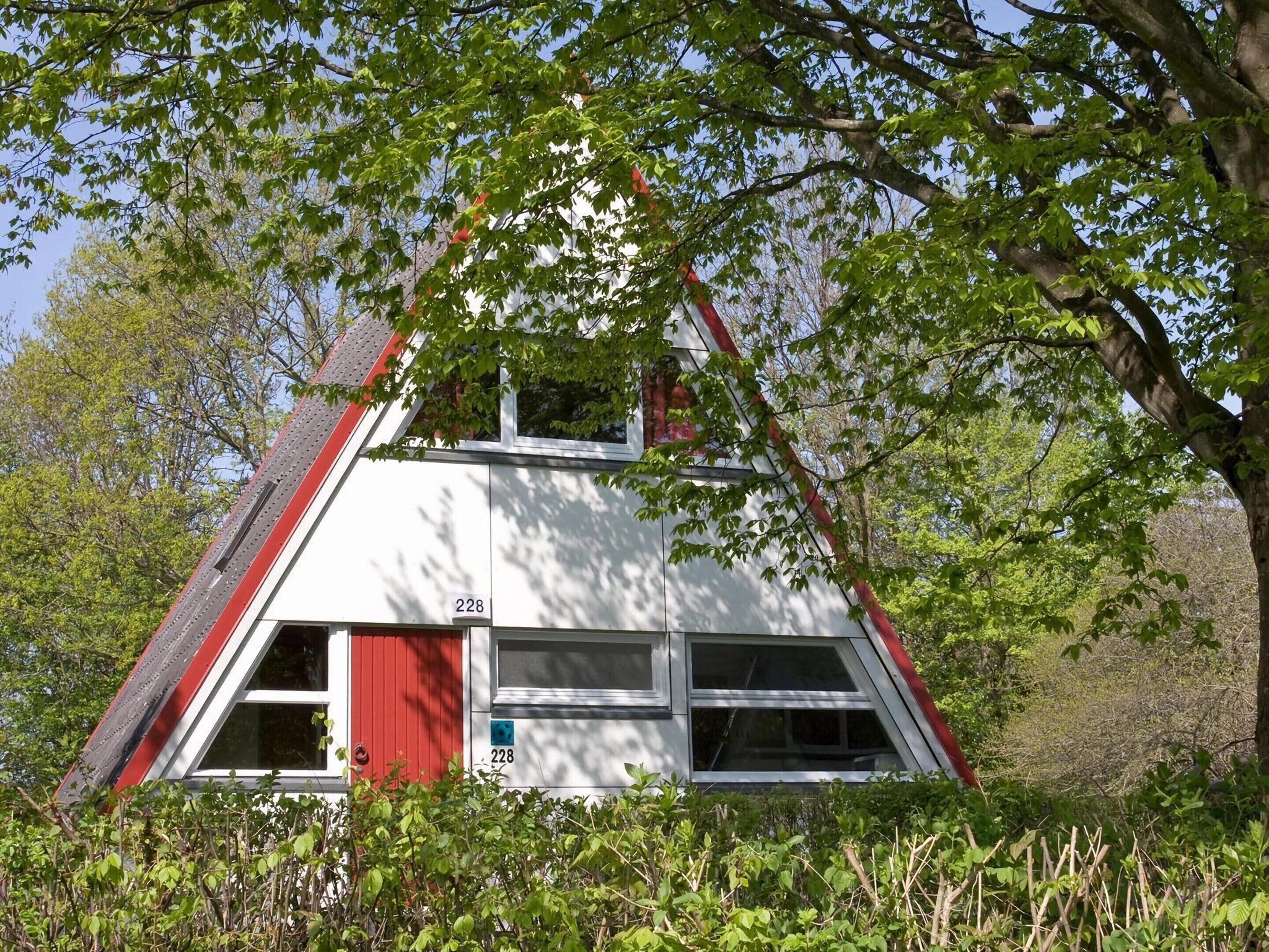 A white house with a red door and windows, surrounded by greenery.