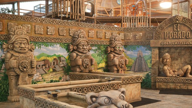 Une fontaine en pierre ornée d’une tête de lion, entourée de sculptures et d’une fresque représentant un temple.
