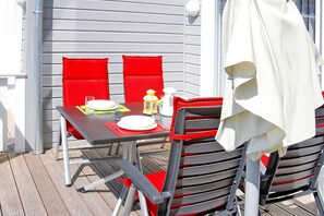 A table set outdoors with red chairs, a white tablecloth, and a white umbrella. - Doppelhaushalfte Rugentraum in Glowe (Glowe)