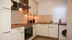 A compact kitchen with white cabinets, a built-in oven, a microwave, a coffee maker, and a washing machine. - Doppelhaushalfte Rugentraum in Glowe (Glowe)