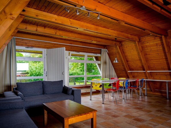 A cozy room with a wooden ceiling, a sofa, a table, and colorful chairs. - Ferienhaus in Damp mit Garten (Damp)