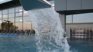 A pool with water flowing from a structure into it, surrounded by lounge chairs and a building with large windows. - Holiday Home in Damp With Garden (Damp)