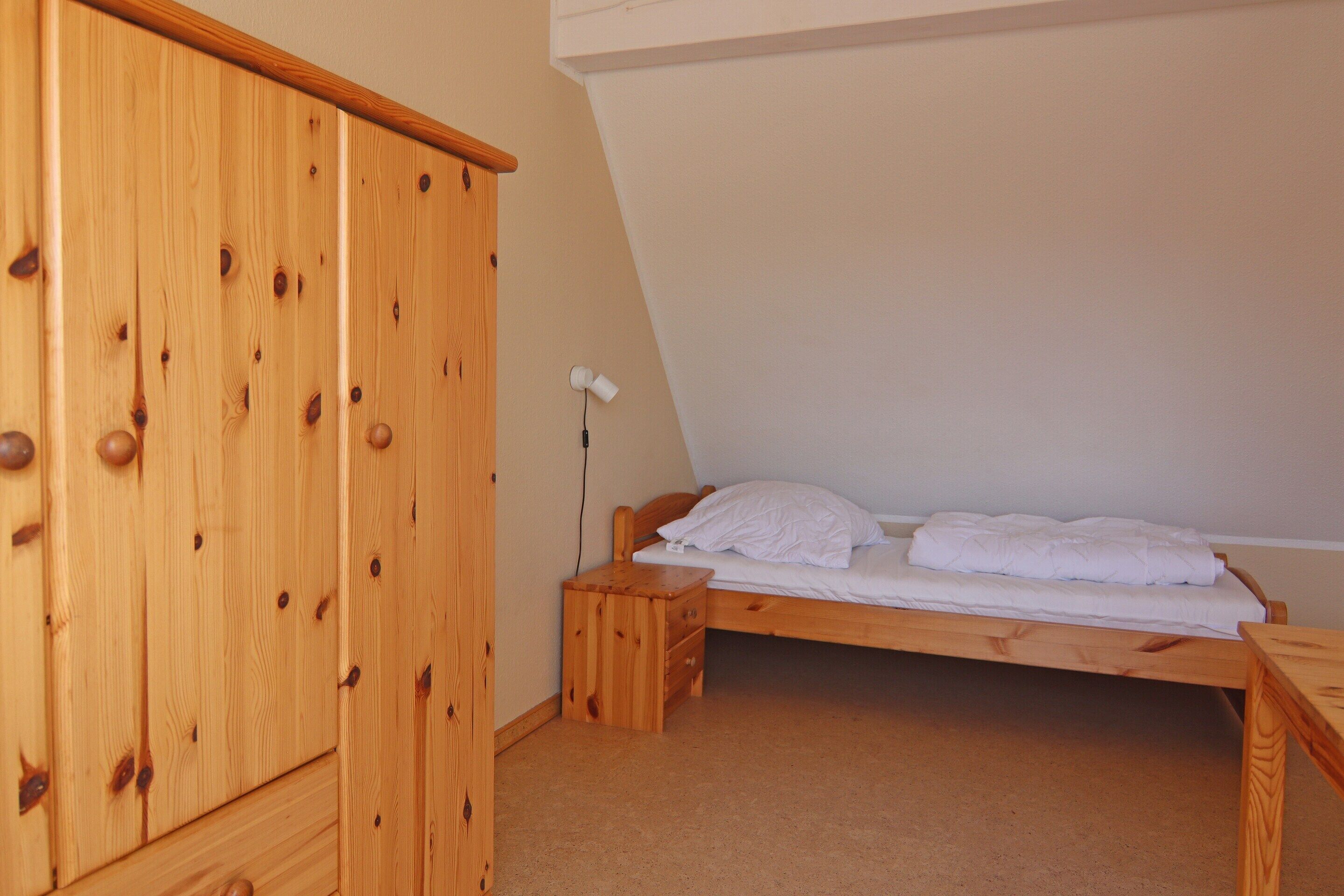 A bedroom with a wooden wardrobe, a single bed with white bedding, and a bedside table.