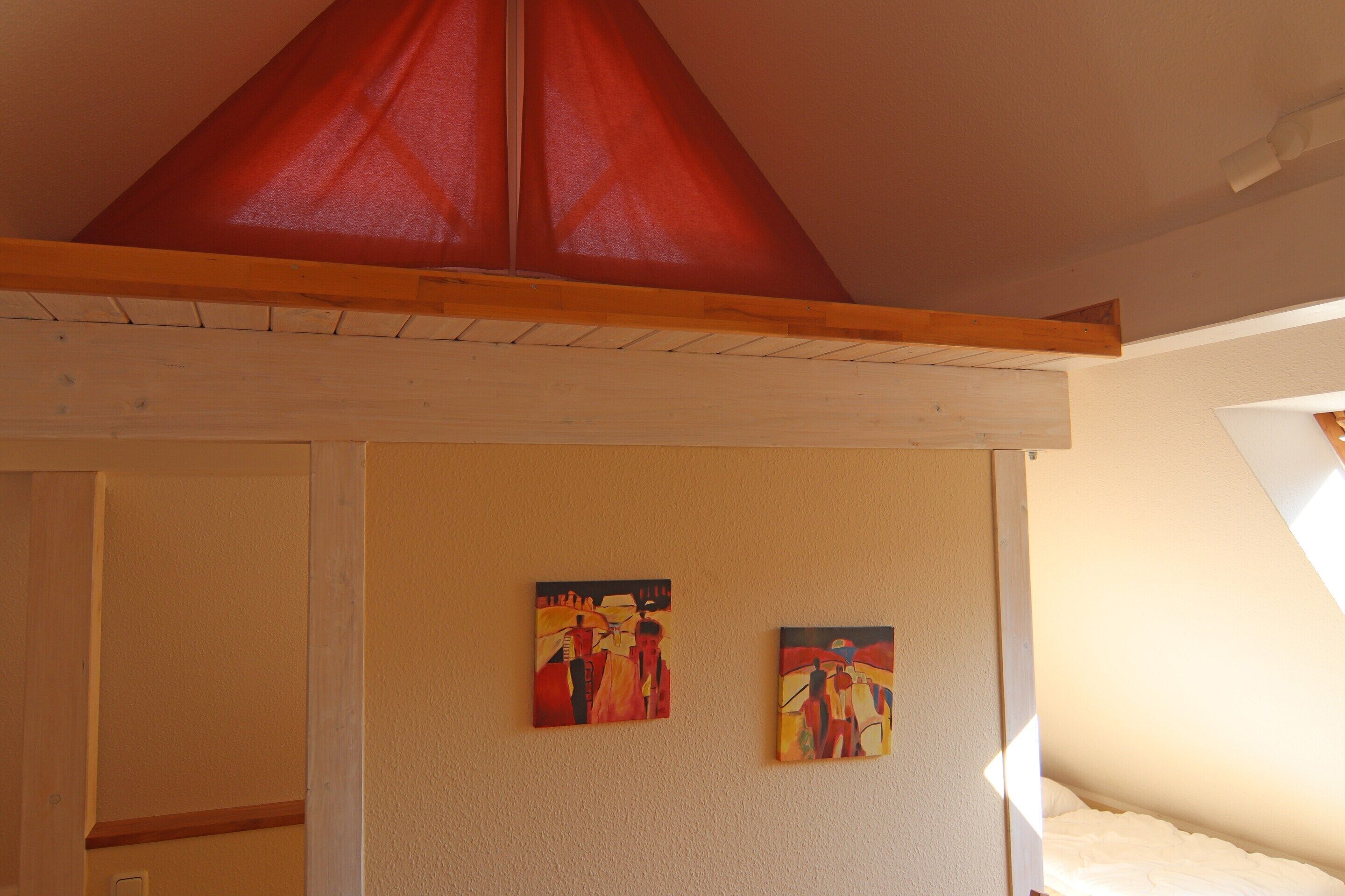 Une pièce avec un plafond en pente, des poutres en bois et deux tableaux accrochés au mur.