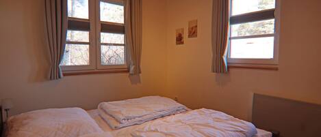 Une chambre avec deux lits, de grandes fenêtres avec des rideaux et un plafond en bois.