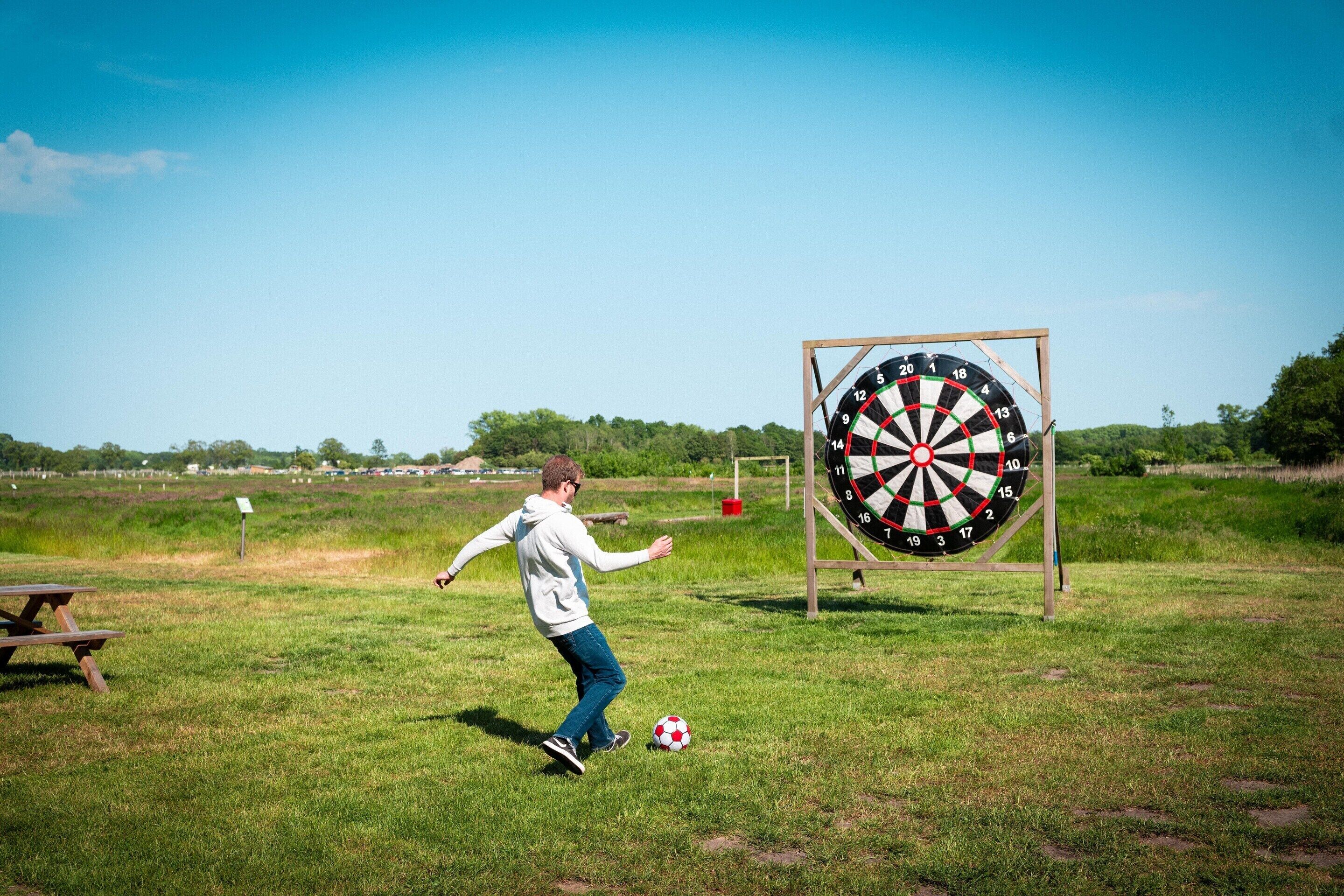 A person playing with a soccer ball in a grassy field with a dartboard in the background.