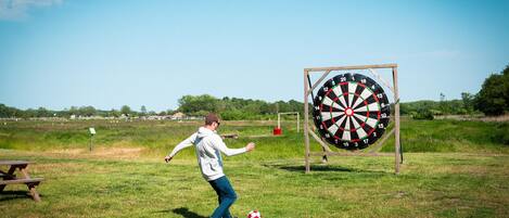 A person playing with a soccer ball in a grassy field with a dartboard in the background.