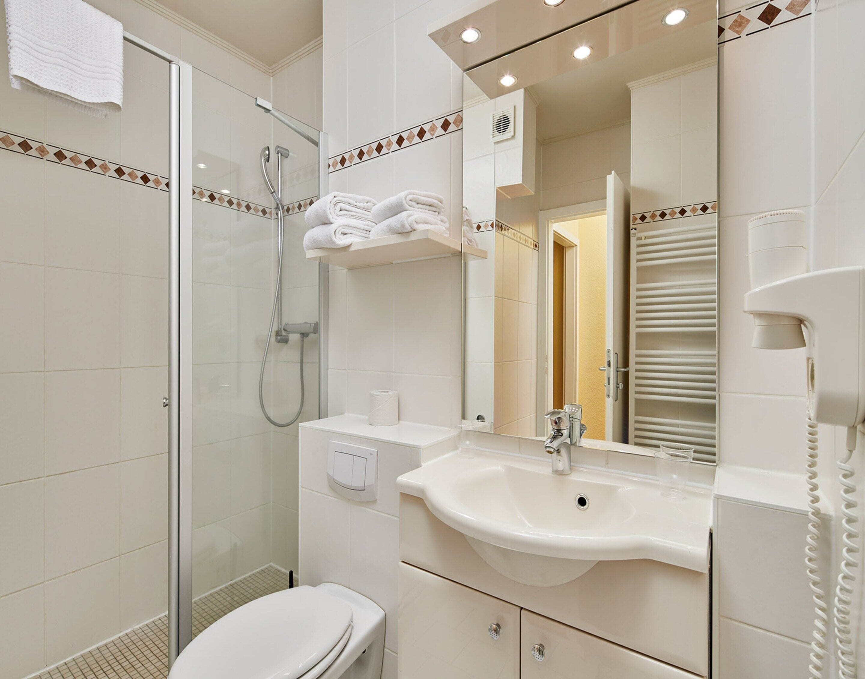 Een moderne badkamer met een douchecabine van glas, een wit wastafelmeubel en een spiegel met een handdoekhouder erboven.