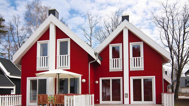 A red two-story house with a white porch and a covered patio area. - Doppelhaushalfte Dunenrose, Glowe (Glowe)