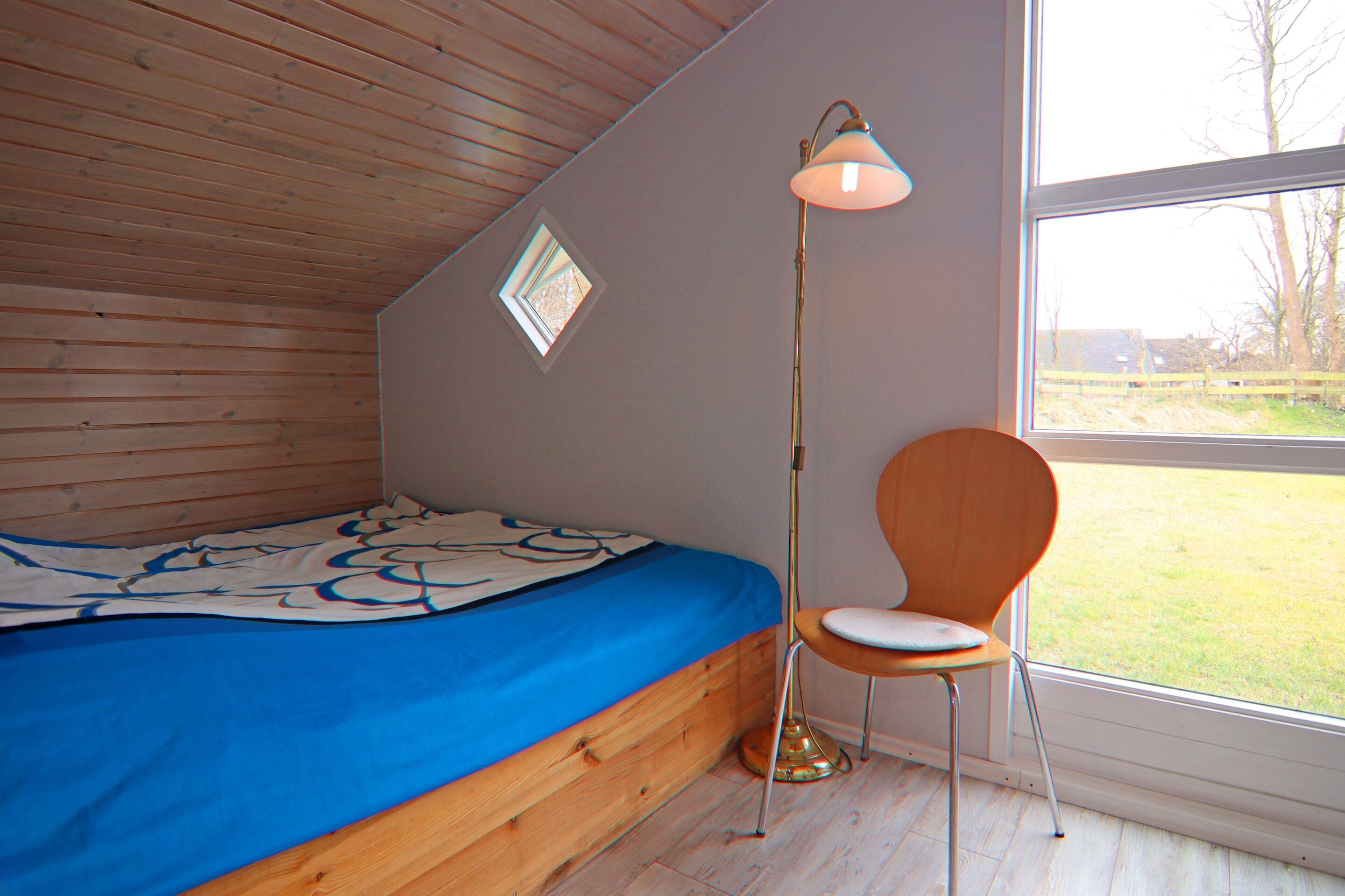 A bedroom with a bed, a chair, a floor lamp, and a window with a view of the outdoors.
