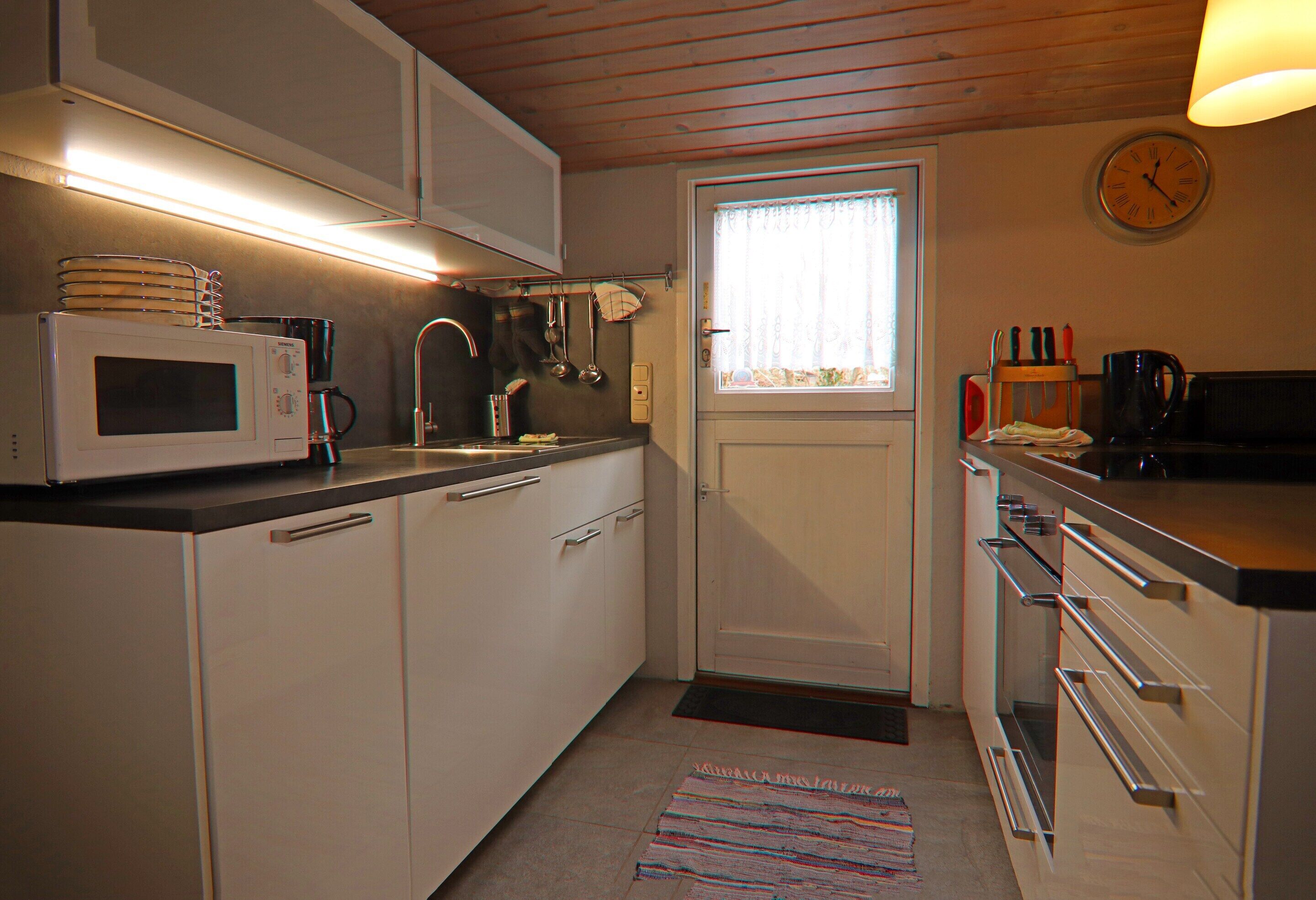 A compact kitchen with white cabinets, a microwave, a sink, and a window with curtains.