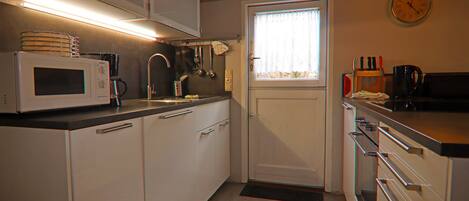 A compact kitchen with white cabinets, a microwave, a sink, and a window with curtains.