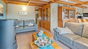 A spacious living area with a wooden ceiling, a grey sofa, a wooden cabinet, and a kitchen in the background. - Charming Apartment Near the Beach (De Haan)