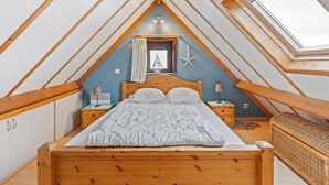A bedroom with a sloped ceiling, wooden beams, a bed, bedside tables, a lamp, a starfish decoration, and a window. - Charming Apartment Near the Beach (De Haan)