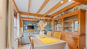A dining area with a wooden table, chairs, and a cabinet with glassware. - Charming Apartment Near the Beach (De Haan)