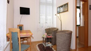 Een woonkamer met een houten tafel, twee stoelen, een bank, een vloerlamp en een televisie aan de muur.