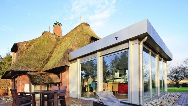 Une maison moderne avec un toit de chaume et une extension en verre.