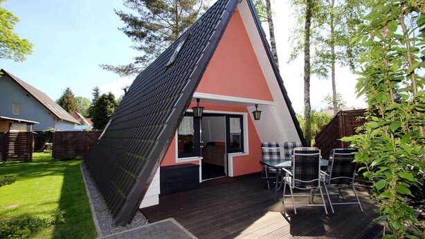 Una casa triangolare con tetto scuro e facciata rossa, dotata di patio con mobili da esterno e ingresso con porta scorrevole in vetro.