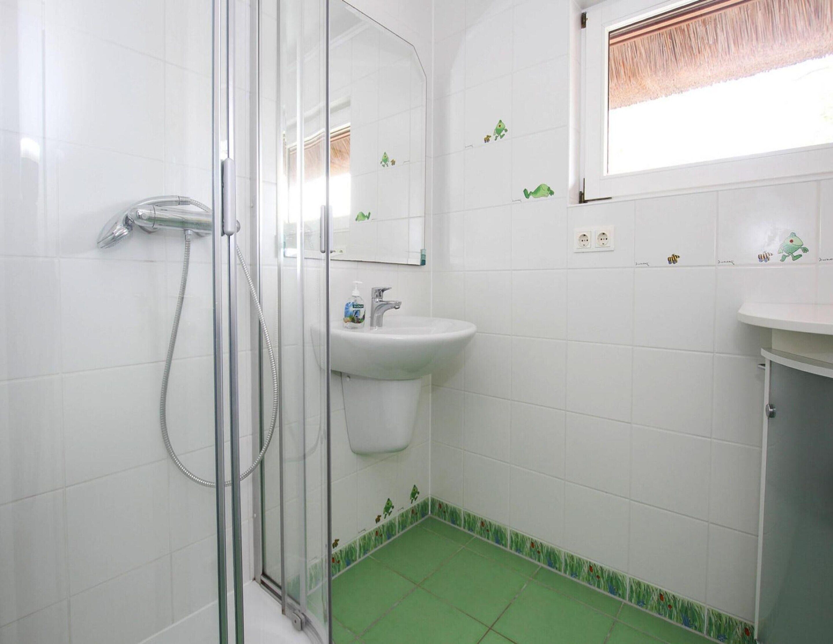 Een badkamer met een douchecabine van glas, een wastafel en een raam met gordijn.