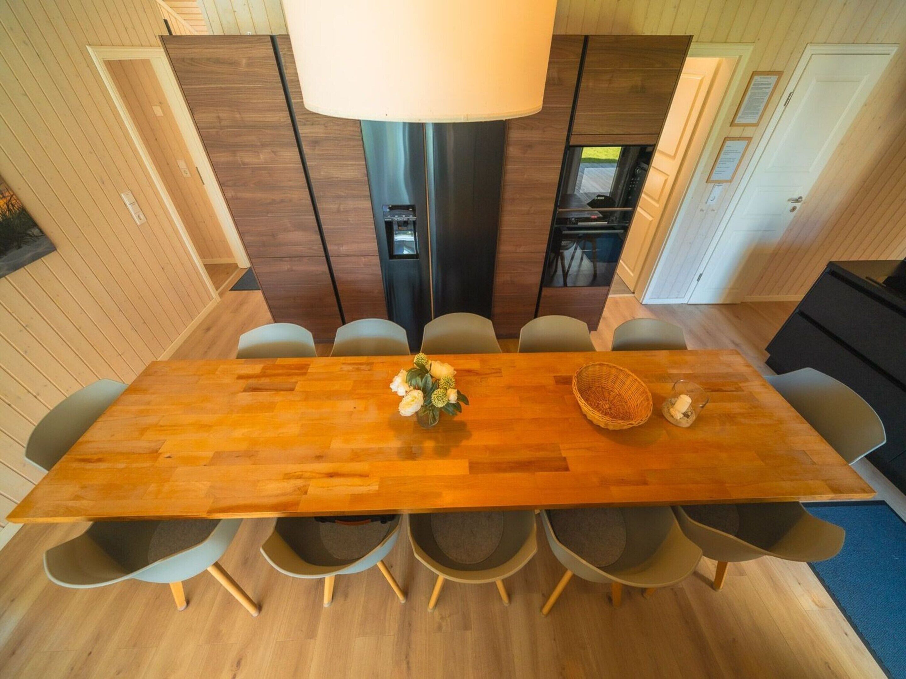 A modern dining area with a wooden table, six chairs, a vase of flowers, and a basket.