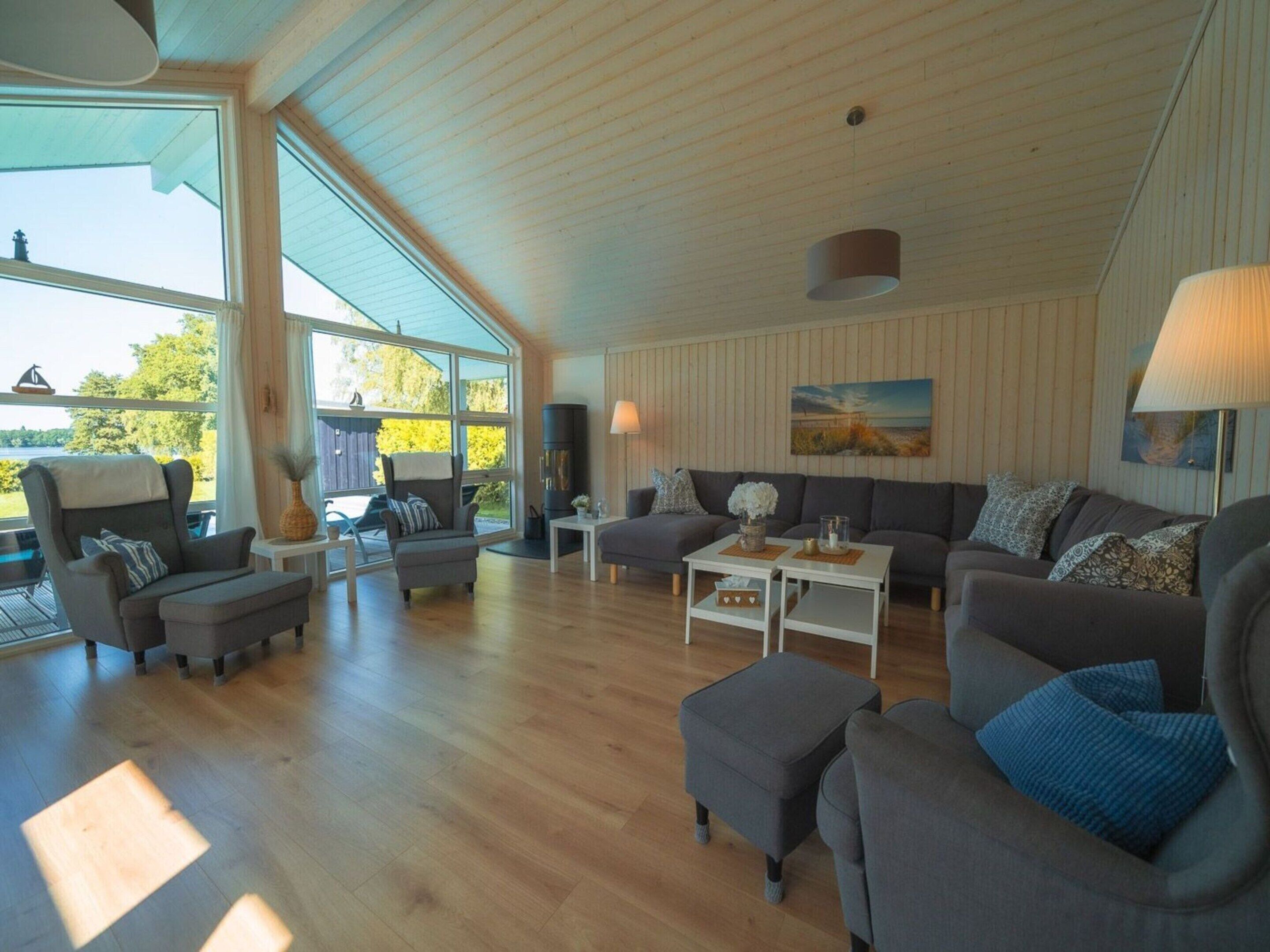 En rummelig stue med højt til loftet, store vinduer og et hyggeligt opholdsområde med sofa og lænestole.