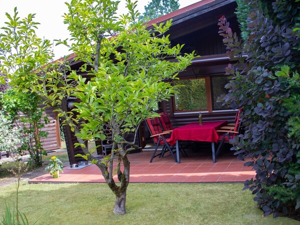 Une cabane en bois avec un patio couvert, une table à manger avec des chaises et un petit arbre au premier plan.