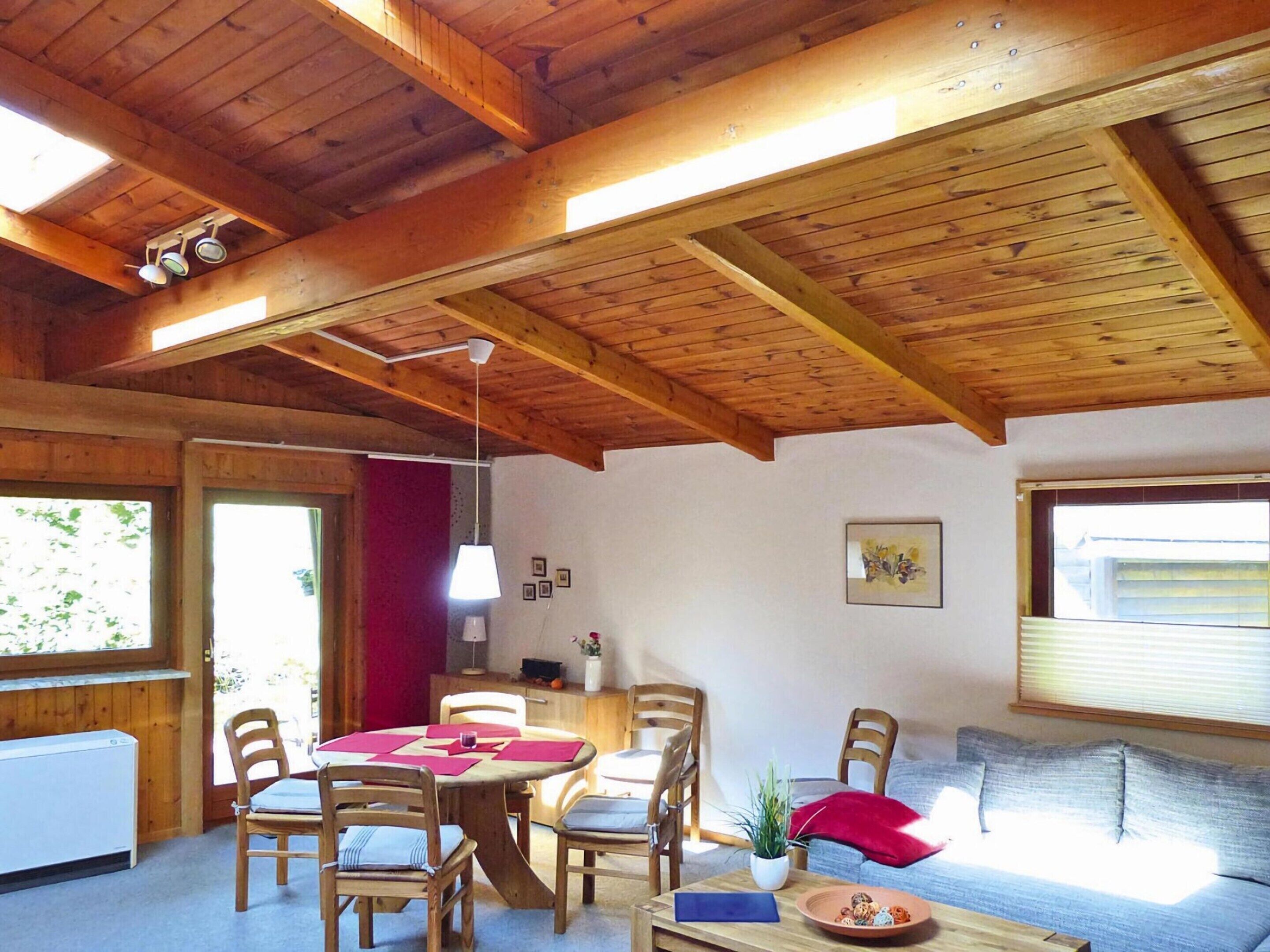 Una habitación acogedora con vigas de madera, una mesa de comedor con sillas, un sofá, un radiador y una ventana con persianas.