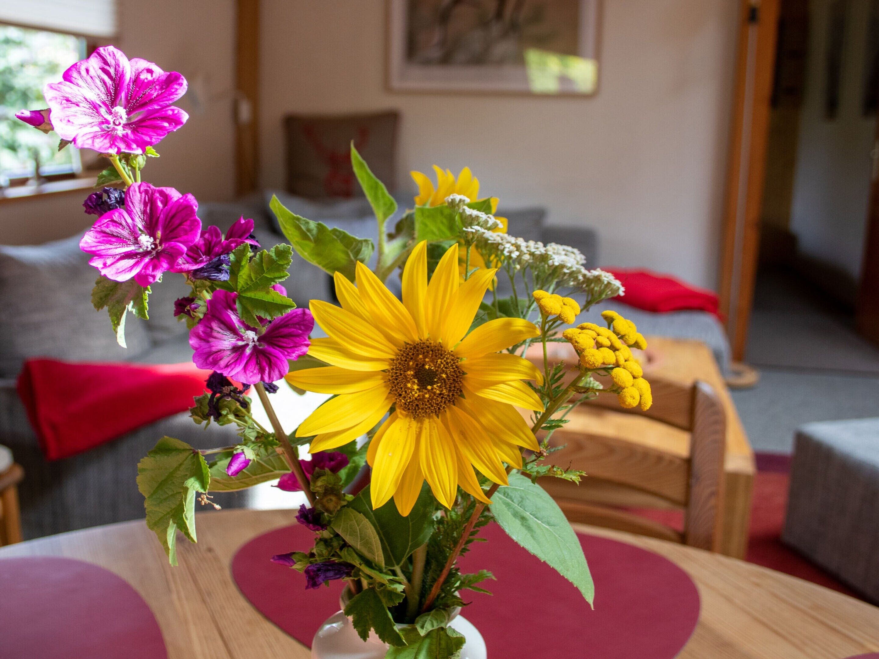 Une pièce avec une table en bois, un coussin rouge et un vase rempli de fleurs.