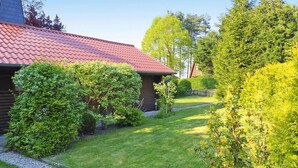 En hytte med røde tegltag, omgivet af velplejede græsplæner og frodig buskads.