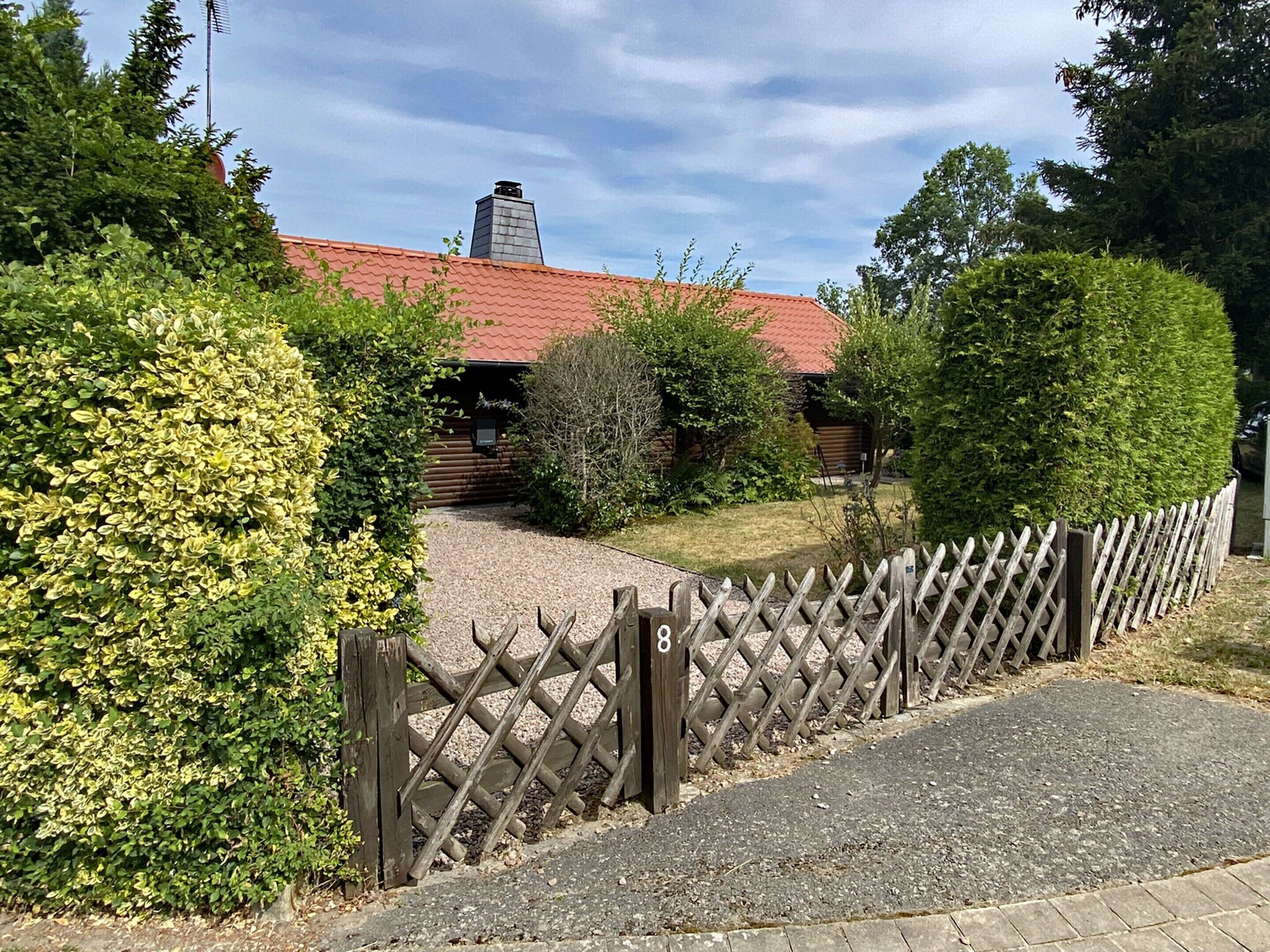 A wooden fence with a gate, a gravel path, and a building with a red roof and chimney.