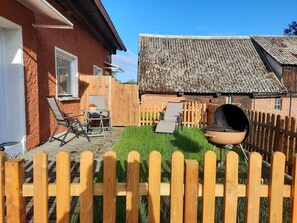 Ein Garten mit Grill, Holzzaun und einem Haus mit Backsteinfassade und Ziegeldach.
