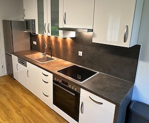 A modern kitchen with white cabinetry, a stainless steel range hood, a built-in oven, and a black stovetop. - Moderne Ferienwohnung Strandidyll, Trassenheide (Trassenheide)
