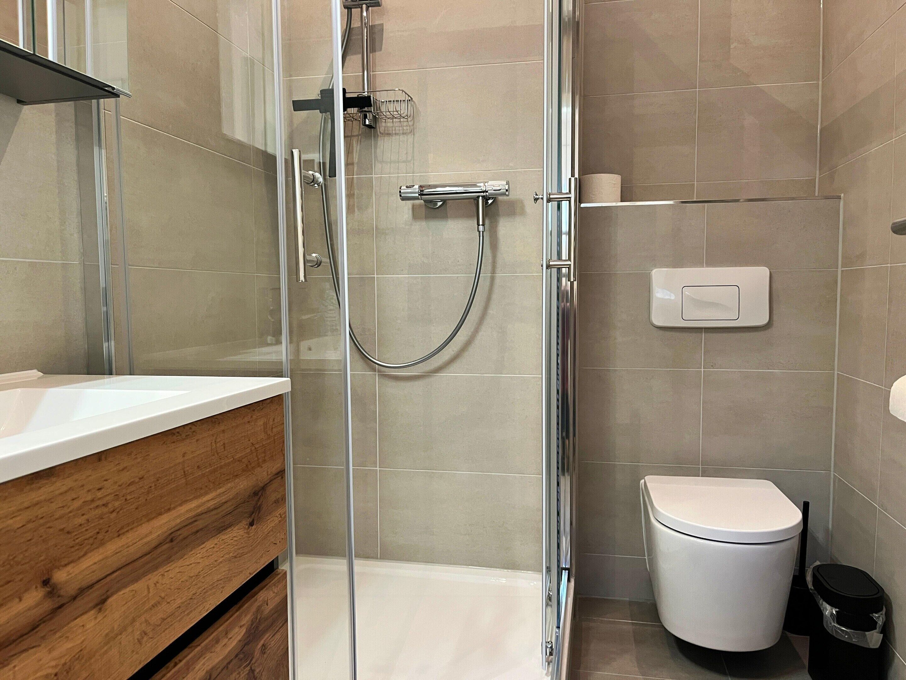 A modern bathroom with a glass shower enclosure, a white toilet, and a wooden vanity.