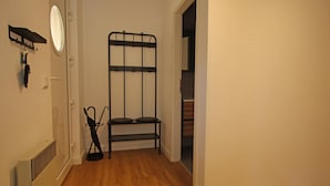 Une pièce avec un radiateur, un miroir, une étagère en métal noir et une porte donnant sur une autre pièce.