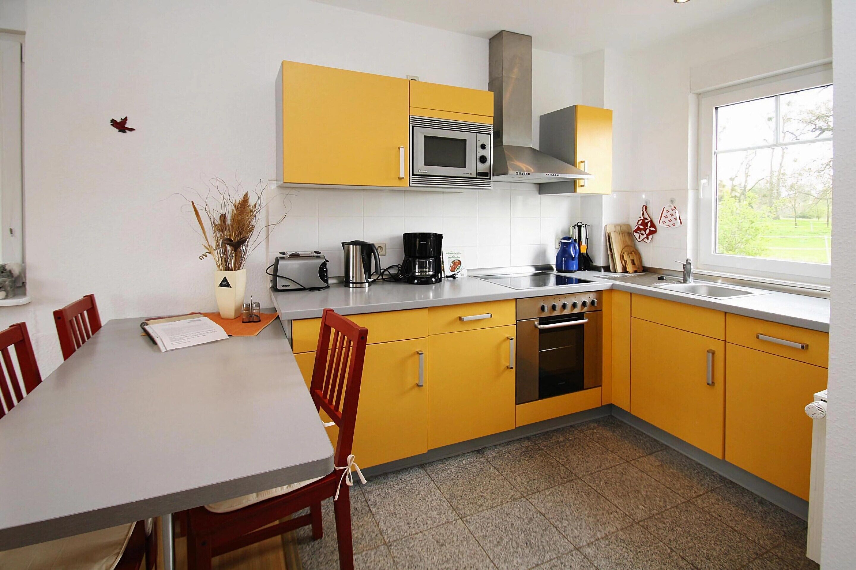 A kitchen with yellow cabinets, a microwave, a stove, and a window with a view of greenery.