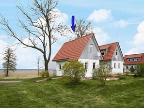 Egy kétszintes ház, vörös cseréptetős, melyet füves udvar és fák vesznek körül.