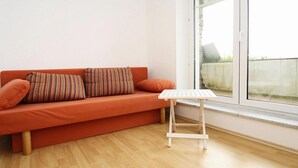 Une pièce avec un plancher en bois, un canapé rouge orné de coussins à rayures et une petite table blanche.