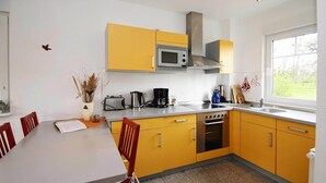 Une cuisine avec des meubles de couleur jaune, un four à micro-ondes, une cuisinière et une fenêtre donnant sur un paysage verdoyant.