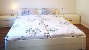 A bedroom with a bed, two bedside tables, a nightstand, a lamp, and a painting on the wall. - Charmantes Ferienhaus mit Kamin in Lintig (Geestland)