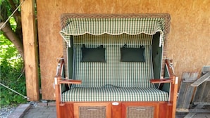 Un siège de balançoire en bois avec un coussin à carreaux, deux panneaux latéraux et un auvent.