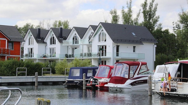 A row of white houses with a balcony, a dock with boats, and a calm water body. - Appartement Hafenflair am Plauer See (Plau am See)