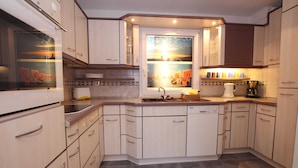 Een moderne keuken met lichte houten kastjes, een centraal eiland met een spoelbak, en een raam met een prachtig uitzicht.
