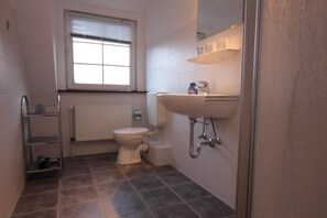 A small bathroom with a toilet, a sink, a window, and a radiator. - Ferienwohnung in Westerland auf Sylt (Sylt)