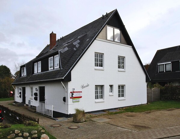 A white building with a black roof, multiple windows, and a sign reading "Ursula". - Ferienwohnung in Westerland auf Sylt (Sylt)